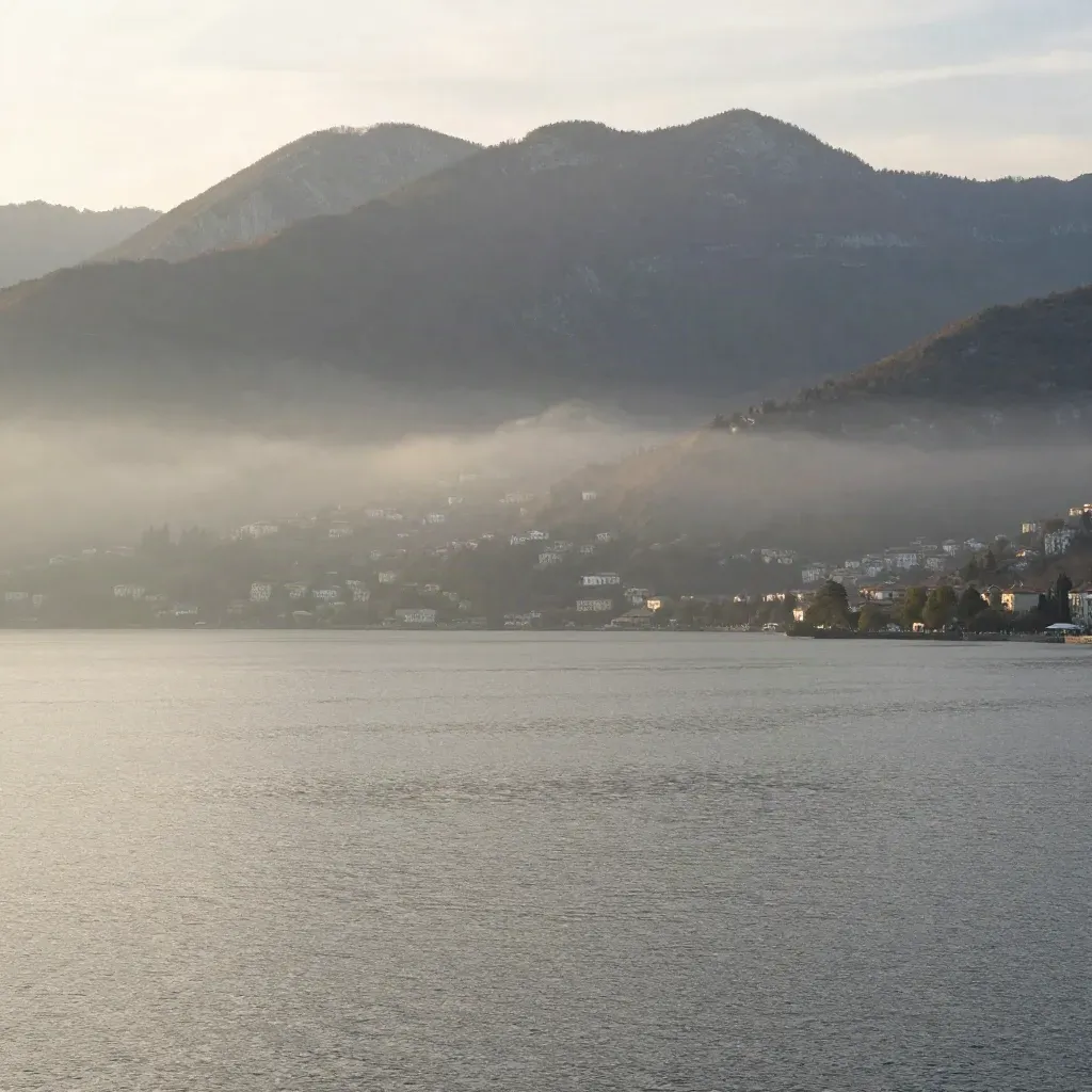 Alba sul lago lombardo con Prealpi velate e nebbia sull’acqua calma